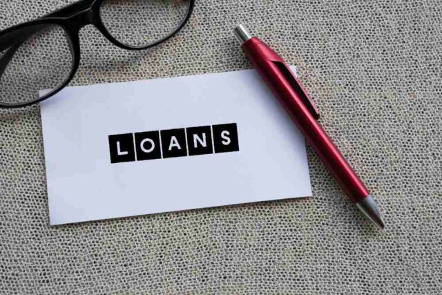 A pair of glasses, a red pen, and a card with the word "LOANS" in bold black letters are placed on a textured surface, hinting at the possibilities offered by Chinatown's money lenders.