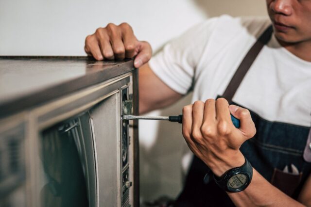 A person wearing a white shirt and apron uses a screwdriver to repair an old television set, showcasing Appliance Solutions for Reliable Repairs and Maintenance Services.